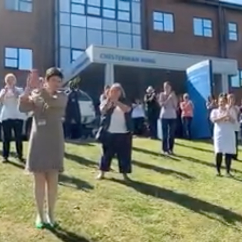 Staff stood socially distanced on grass outside hospital clapping