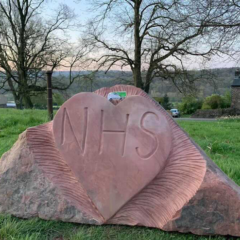 A big rock in a park with a love heart carved into it, and "NHS" etched into the middle of the love heart.