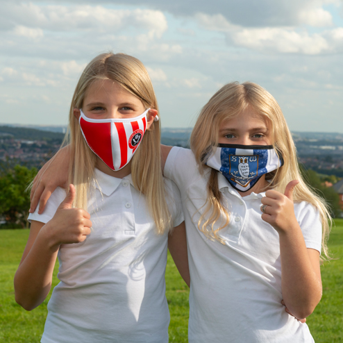 Two school girls looking at camera with thumbs up, one with a Sheffield United face mask, one with a Sheffield Wednesday face mask.