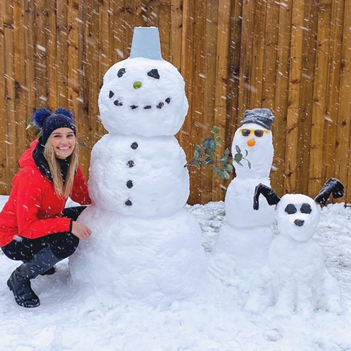 A lady crouching next to a snow-man, snow-child and snow-dog