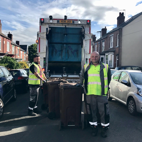 Two bin men stood with wheelie bins behind a bin lorry