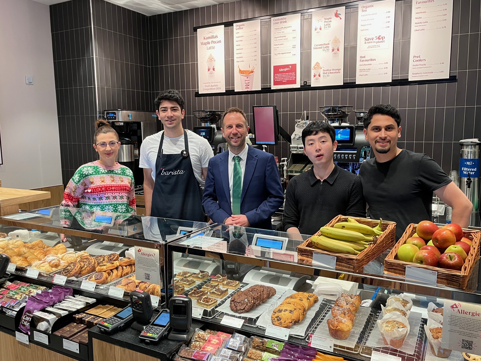 Cllr Ben Miskell stands behind the counter of Pret A Manger with staff members on either side of him and products in front.