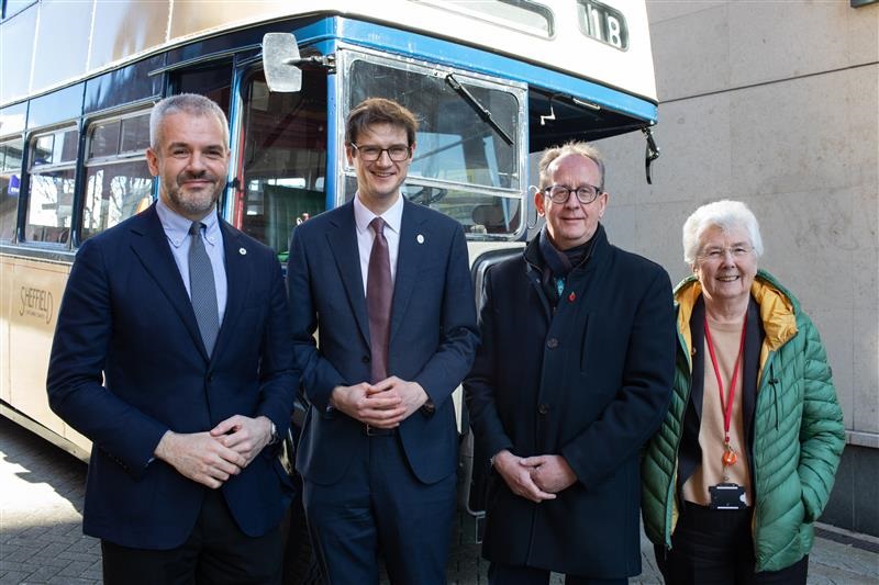 Four people are stood in front of a vintage bus smiling at the camera.