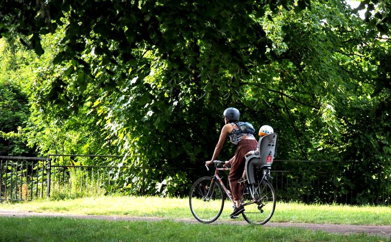 A person cycling in a park with a young child in a backseat