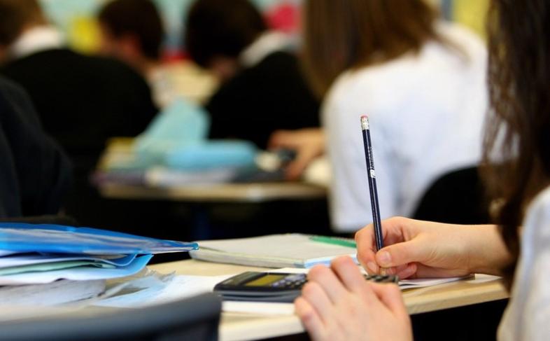 Classroom with a closeup of a students desks and hands holding and writing with a pencil - classmates blurred in the background