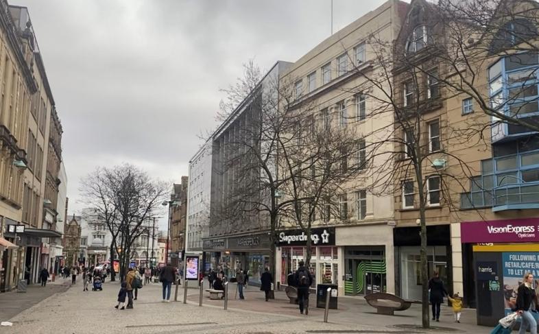 view down fargate with beige buildings surrounding the street with shops and people walking