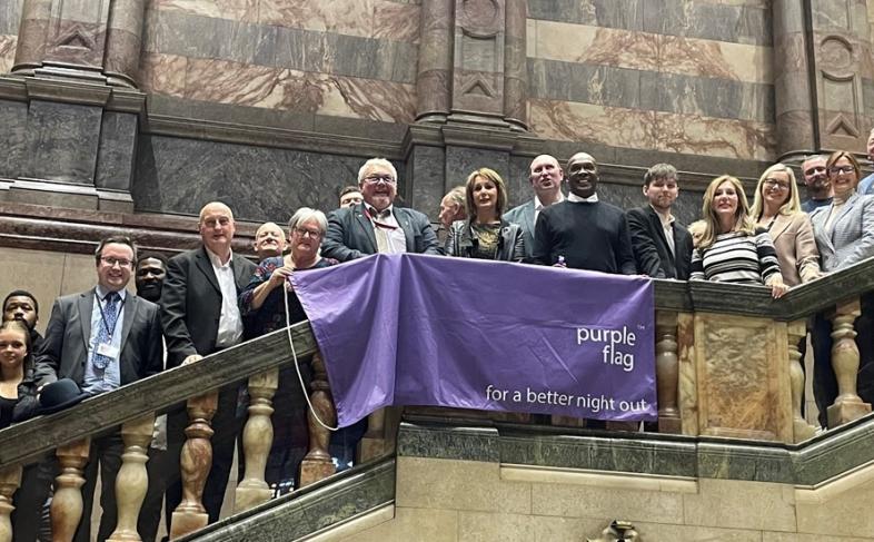 Looking up towards a purple flag hung from the staircase of the Town Hall entrance, with people standing on the stairs