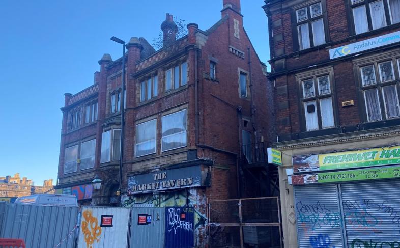 Image of the Tavern Pub with boarding round it. There is graffiti on the building