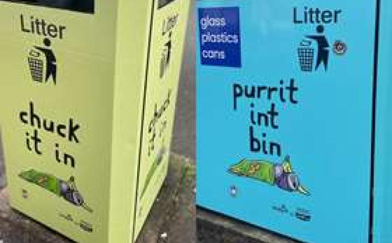 A spliced photograph of two bins, each stood on a pavement. One is painted green and says 'chuck it in' and one is painted blue and says 'purrit int bin'