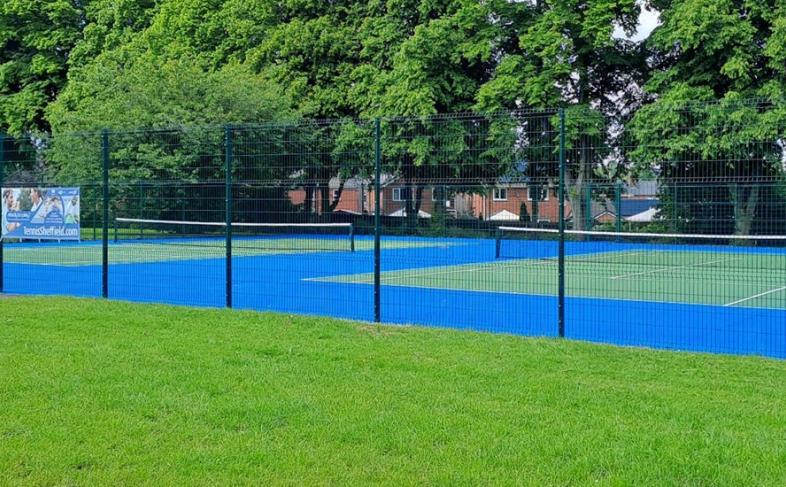 The hard courts at Ecclesfield Park surrounded by a fence and grasss with trees in the background