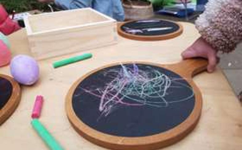 A child picks up a blackboard they have scribbled colourfully all over