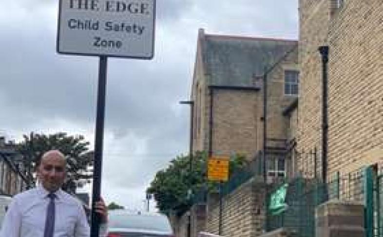 Cllr Mazher Iqbal next to a road sign that says 'THE EDGE Child Safety Zone'