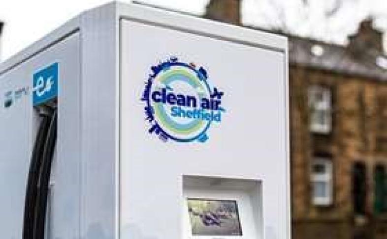 A grey EV charger on a city street with a house in the background which says 'clean air Sheffield' on it