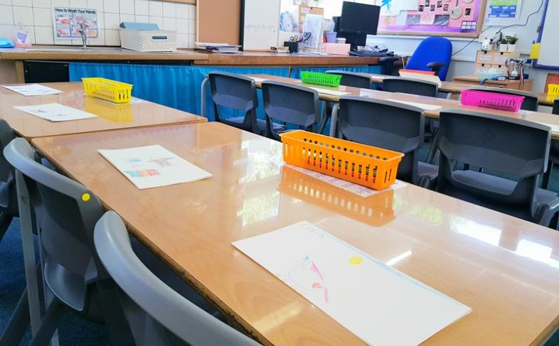 An empty school classroom with a close up view of student's tables and chairs with paper on top