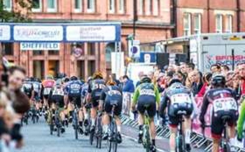 Cyclists compete in a road race in Sheffield as spectators cheer them on, on a sunny day