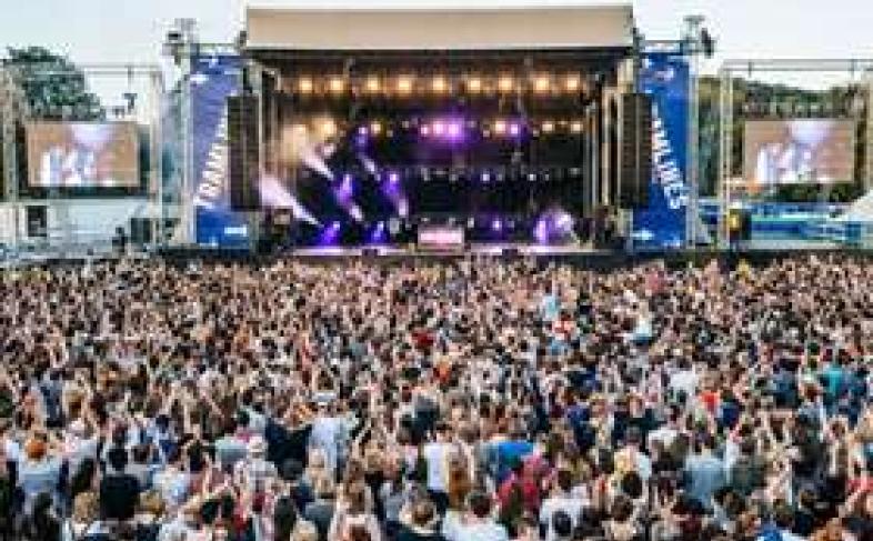 A packed crowd at Tramlines watch a performer under a cloudy sky as the stage lights shine brightly