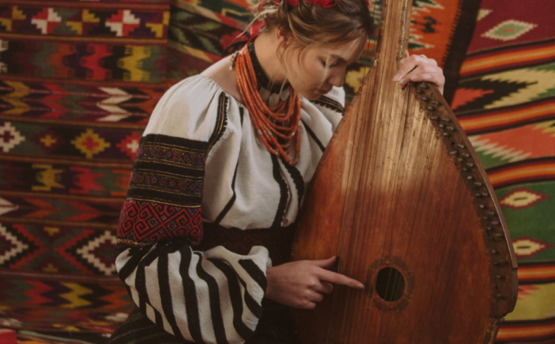 A young woman bows her head against a native Ukrainian guitar while she is wearing traditional Ukrainian dress