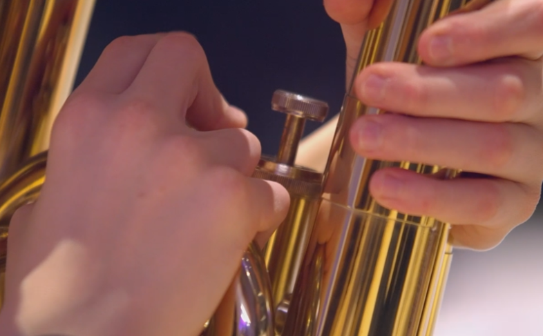 A person playing a brass instrument, holding it with both hands.