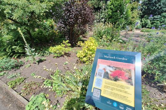 New sign in Sheffield Botanical Gardens in a bed of leaves and flowers with bushes in the background