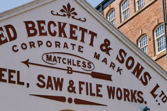 Image of the front of the Beckett Works building. A cream frontage with black lettering. There is a brick building in the background with lots of windows