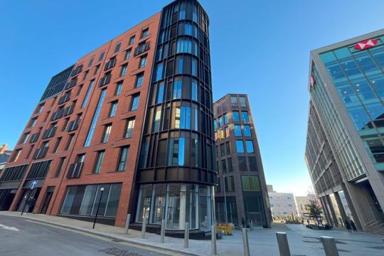 Image of a tall corner building known as the Burgess Building. The building is made of red brick with many glass windows