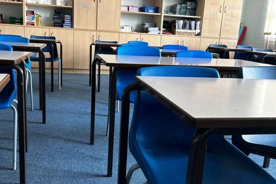 Classroom in a school, blue tables and chairs with cabinets in the background