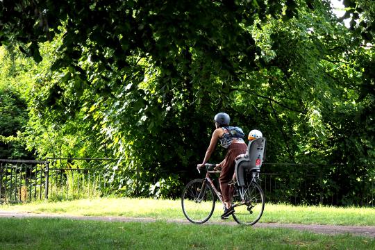 A person cycling in a park with a young child in a backseat