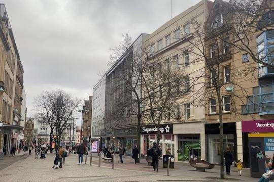 view down fargate with beige buildings surrounding the street with shops and people walking