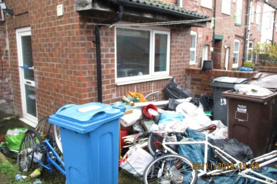 A house with a front garden full of hazardous items including and old bike and bags of rubbish