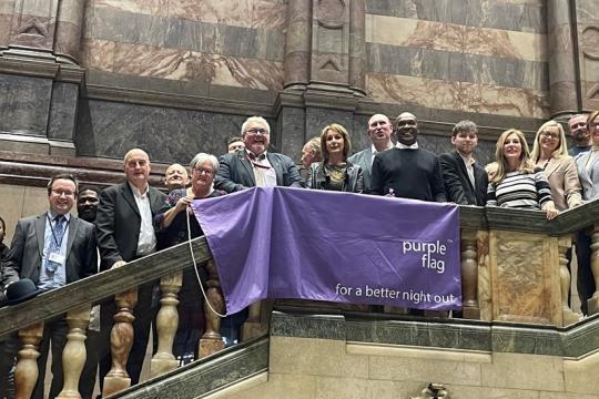 Looking up towards a purple flag hung from the staircase of the Town Hall entrance, with people standing on the stairs