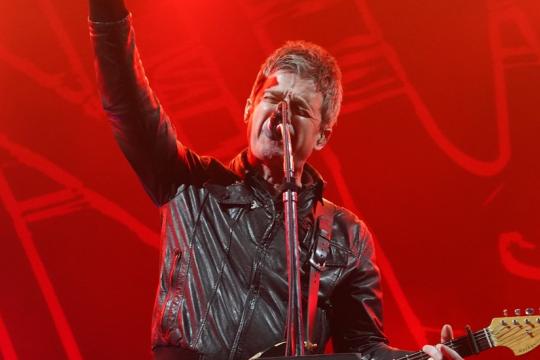 Noel Gallagher on stage with red lighting