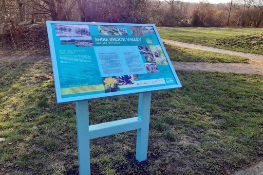 Blue sign for Shire Brooke Valley Nature Reserve with grass and trees in the background