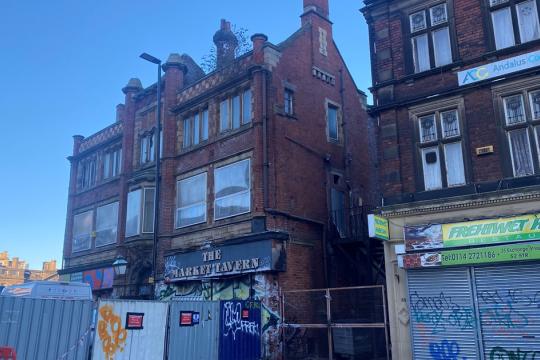 Image of the Tavern Pub with boarding round it. There is graffiti on the building