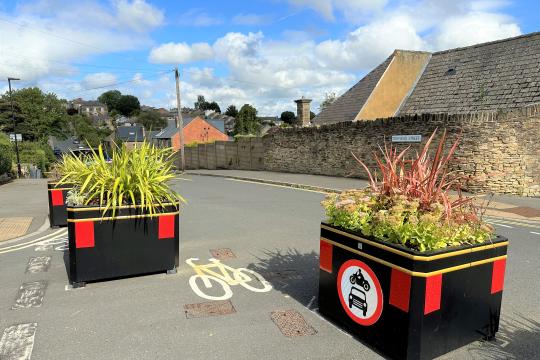 3 black planters in a road, with a no motorised vehicles sign on the side