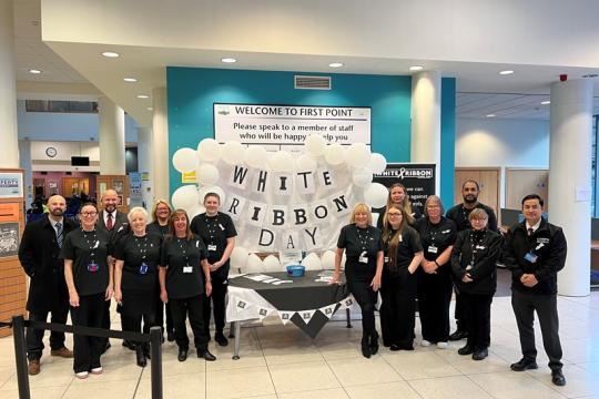 A group of people dressed in black stood around a table with balloons and leaflets 