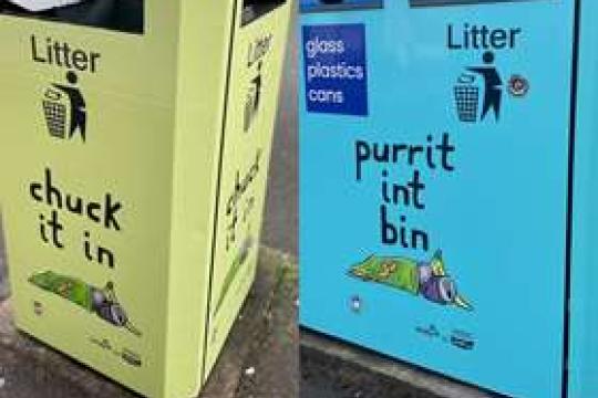 A spliced photograph of two bins, each stood on a pavement. One is painted green and says 'chuck it in' and one is painted blue and says 'purrit int bin'