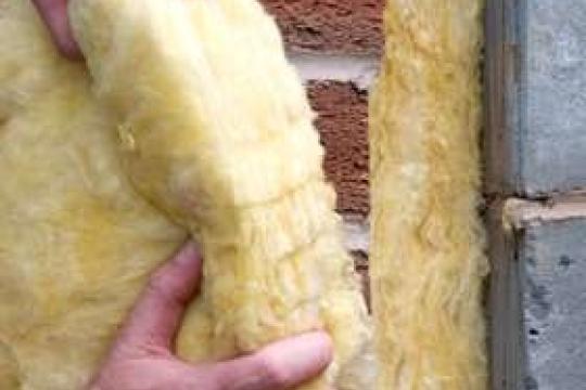 A pair of hands install cavity insulation against a wall