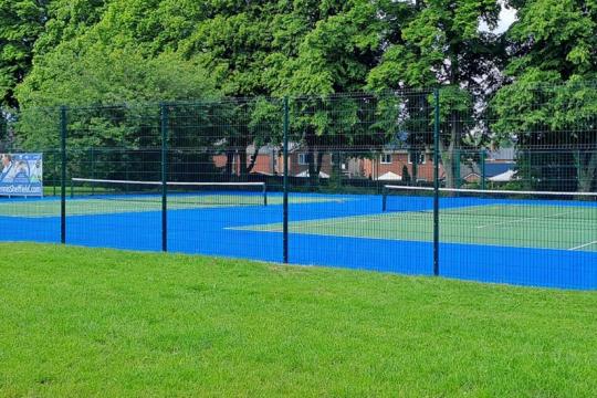 The hard courts at Ecclesfield Park surrounded by a fence and grasss with trees in the background