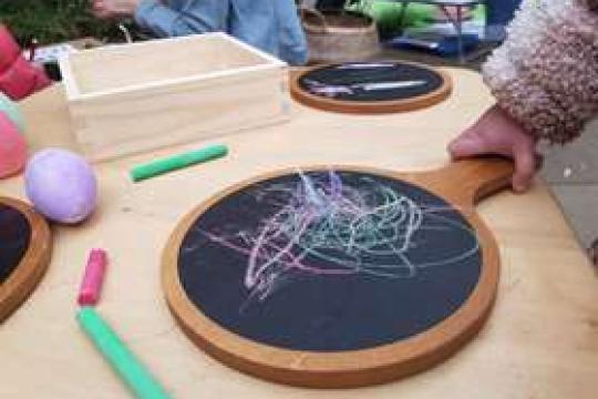 A child picks up a blackboard they have scribbled colourfully all over