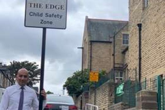 Cllr Mazher Iqbal next to a road sign that says 'THE EDGE Child Safety Zone'