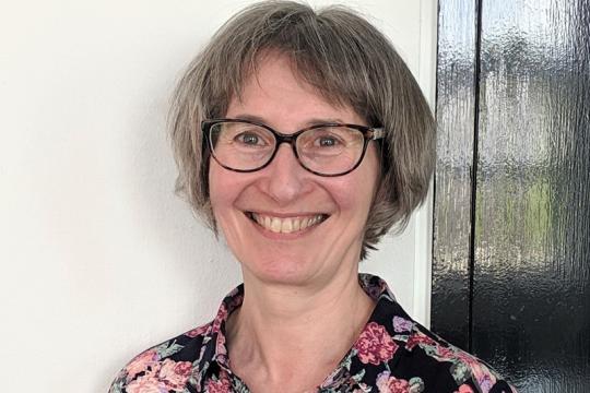 A head and shoulders shot of Mel Kanarek as Mel smiles into the camera while standing in front of a doorframe