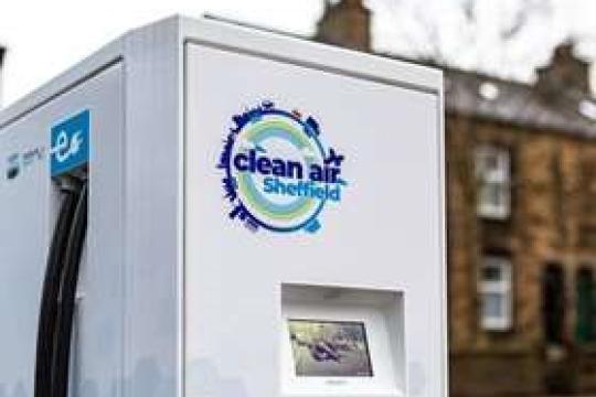 A grey EV charger on a city street with a house in the background which says 'clean air Sheffield' on it