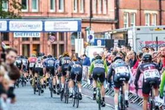 Cyclists compete in a road race in Sheffield as spectators cheer them on, on a sunny day