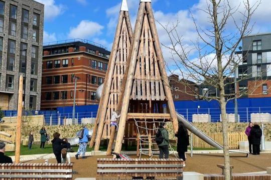 A picture of Pounds Park children's play area under a blue sky with white clouds and surrounded by taller buildings