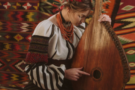 A young woman bows her head against a native Ukrainian guitar while she is wearing traditional Ukrainian dress