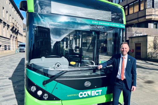 Cllr Ben Miskell stands in front of a green Sheffield Connect electric bus on a beautiful sunny day.