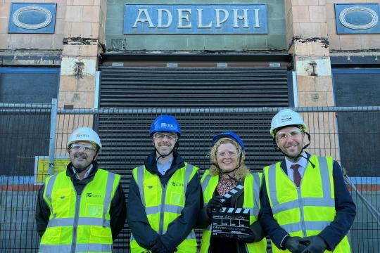 Four people in highvisibility jackets and hardhats stand outside the former Adelphi Cinema building with the sign above them saying Adelphi