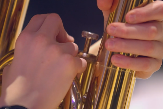 A person playing a brass instrument, holding it with both hands.