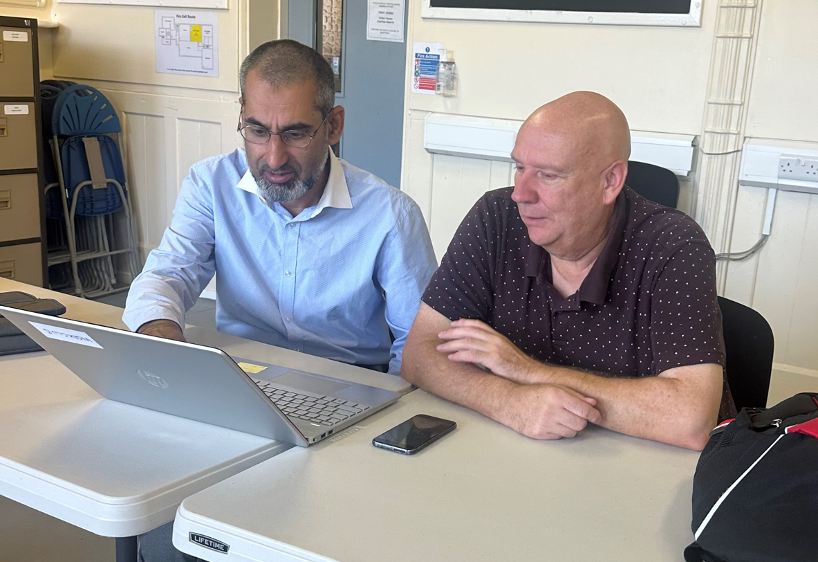 2 people sitting at a desk looking at a laptop screen